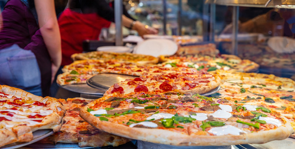 Sortiment italienischer Pizzen in einem Schaufenster. Arbeiterinnen servieren die Pizzen. - Foto, Bild