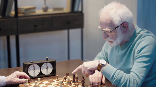 gedeeltelijke weergave van twee peinzende Senior mannen spelen Schaken, gebaren en het indrukken van de knop op de schaak klok aan tafel - Video