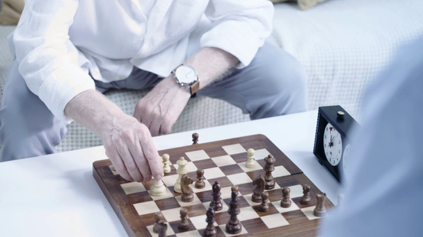 kaksi vanhempaa miestä pelaa shakkia yhdessä olohuoneessa
 - Materiaali, video