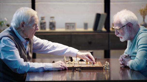 вид сбоку двух застенчивых старших мужчин, играющих в шахматы и нажимающих кнопку на шахматные часы за столом
 - Кадры, видео