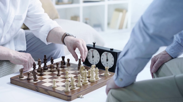 Teilansicht zweier älterer Männer beim Schachspielen und Knopfdruck auf die Schachuhr am Tisch - Filmmaterial, Video