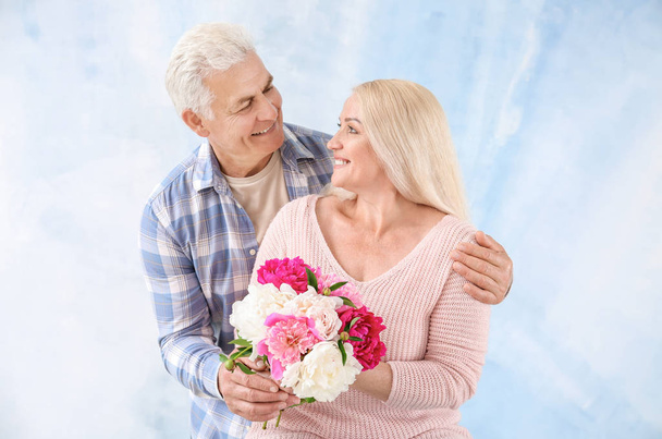 Portrait of happy mature couple with flowers on color background - Foto, afbeelding