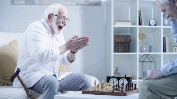 bearded senior man in glasses playing chess, rubbing hands, laughing and shaking hands with opponent - Footage, Video