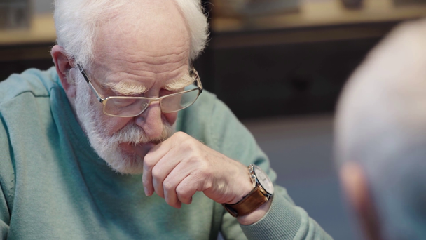 pensive bearded senior man in glasses looking down while sitting near friend - Footage, Video