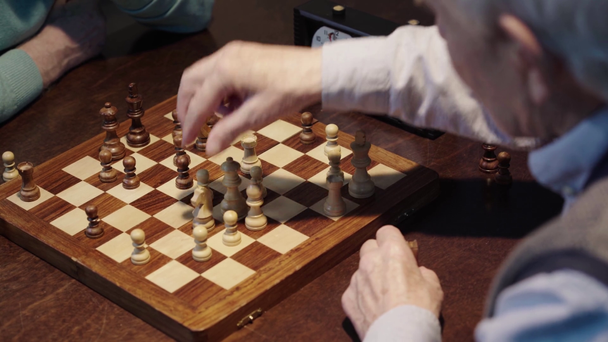 μερική θέα δύο ηλικιωμένων ανδρών παίζοντας σκάκι και πατώντας το κουμπί στο σκάκι ρολόι στο ξύλινο τραπέζι - Πλάνα, βίντεο