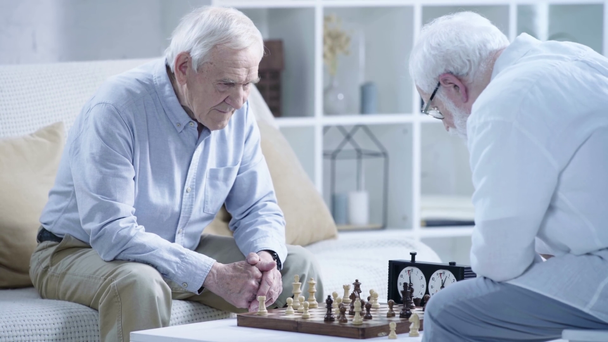 zwei nachdenkliche ältere Männer beim Schachspielen und Drücken der Taste auf der Schachuhr im Wohnzimmer - Filmmaterial, Video