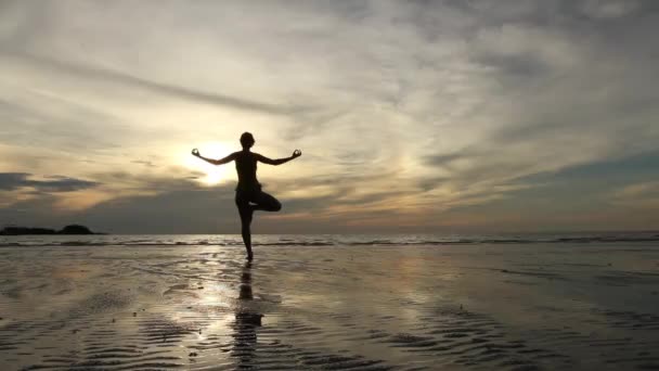 Молода жінка практикує йогу на пляжі на заході сонця
 - Кадри, відео