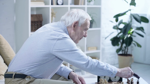 Widok z boku zamyślony starszy człowiek gra w szachy z przeciwnikiem i naciskając przycisk na Zegar szachowy - Materiał filmowy, wideo