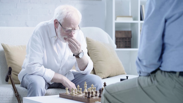 Ausgeschnittene Ansicht zweier nachdenklicher älterer Männer, die Schach spielen und Knopf an der Schachuhr drücken - Filmmaterial, Video