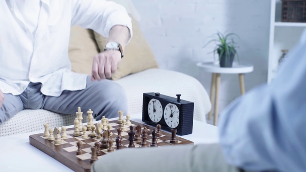Ausgeschnittene Ansicht zweier älterer Männer, die im Wohnzimmer Schach spielen - Filmmaterial, Video