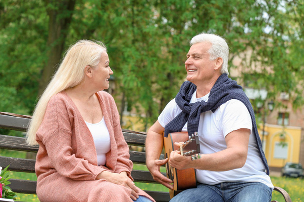 Homme mûr jouant de la guitare pour sa femme dans le parc
 - Photo, image