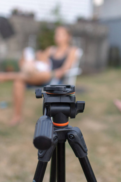 An empty black tripod looking towards a blurred women and child outdoors for a photography shoot. Conceptual. - Foto, immagini