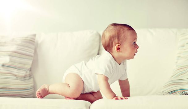 little baby in diaper crawling along sofa at home - Fotoğraf, Görsel