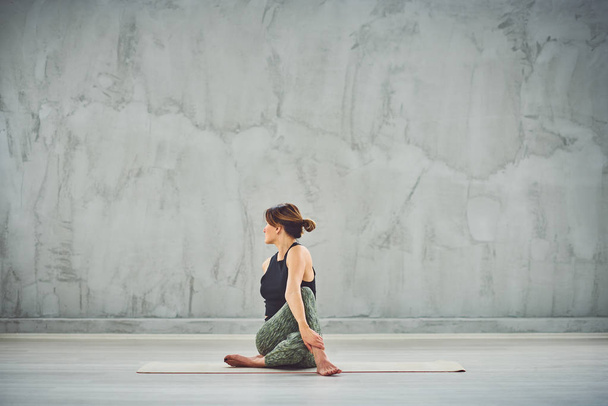 Красивая брюнетка-кавказка в спортивной одежде, сидящая в позе йоги Сейдж Маричи
. - Фото, изображение
