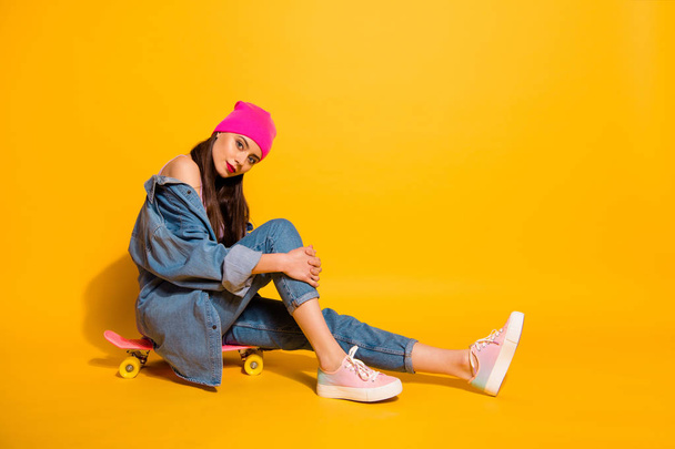 Full length side profile body size photo beautiful she her lady weekend vacation sporty free time sitting own skate board wear casual jeans denim jacket shoes pink hat isolated yellow vivid background - 写真・画像