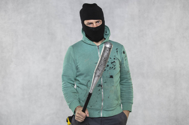 a masked hooligan holds a baseball bat in his hand - Фото, зображення