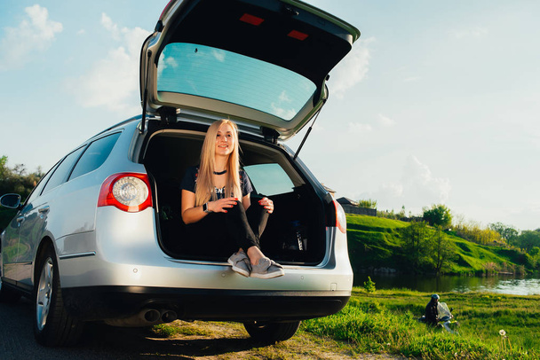 portrait of beautiful young woman sitting in car trunk on nature - Фото, зображення