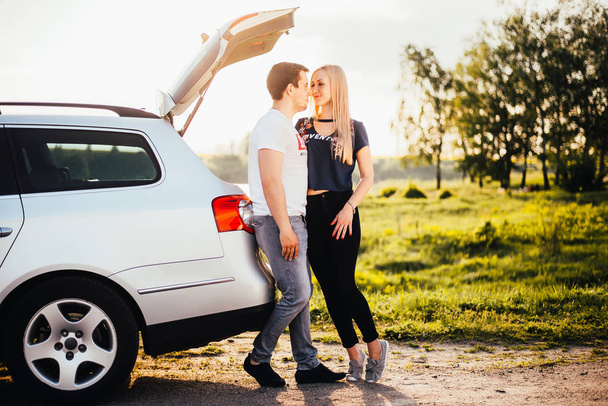 beautiful young couple standing near car trunk together during trip - Fotó, kép
