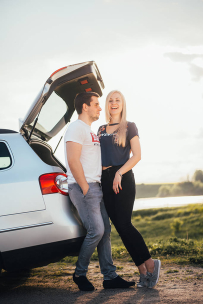 beautiful young couple standing near car trunk together during trip - Zdjęcie, obraz