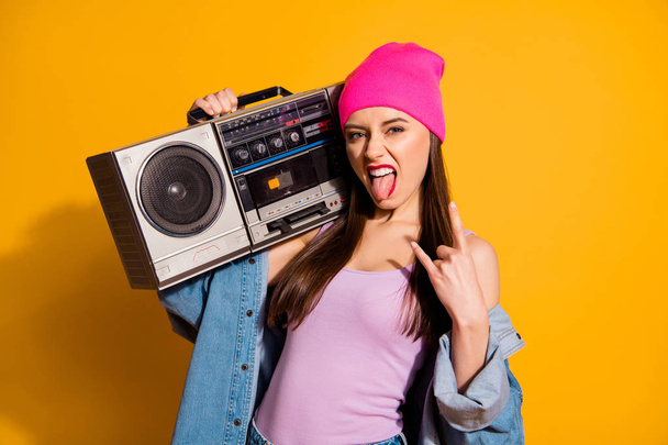 Close up photo funny she her lady hold vintage audio recorder shoulder tongue out mouth brutal metal concert fan rest relax wear casual jeans denim jacket pink hat isolated yellow bright background - Fotografie, Obrázek