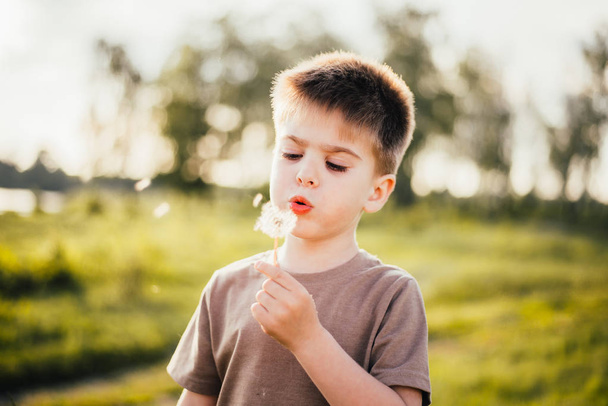 portrait of cute kid blowing out dandelion flower outdoors - Fotó, kép