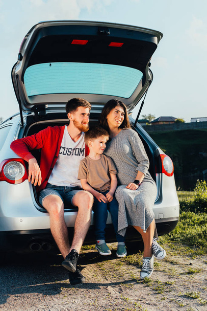 beautiful young family sitting in car trunk on nature - Foto, afbeelding