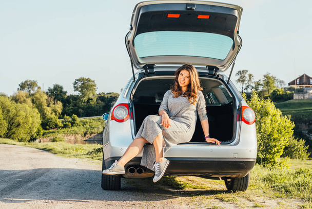 portrait of beautiful young woman sitting in car trunk on nature - Fotografie, Obrázek
