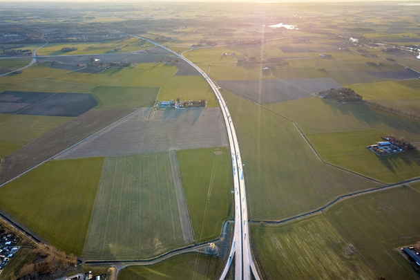 Vista aérea superior da paisagem rural, estrada rodoviária moderna e pequenos edifícios agrícolas no fundo do campo verde primavera. Fotografia de drones
. - Foto, Imagem