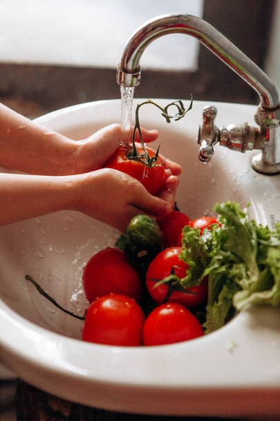 child washes vegetables under running water sink - Photo, Image