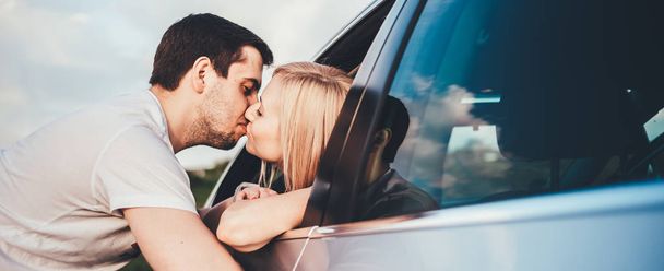 beautiful young couple kissing through car window during trip - 写真・画像
