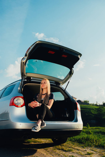 portrait of beautiful young woman sitting in car trunk on nature - Фото, зображення
