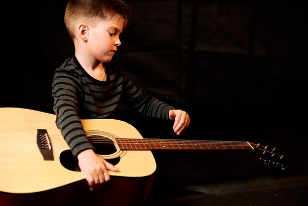 portrait of adorable kid playing guitar on black - Foto, afbeelding