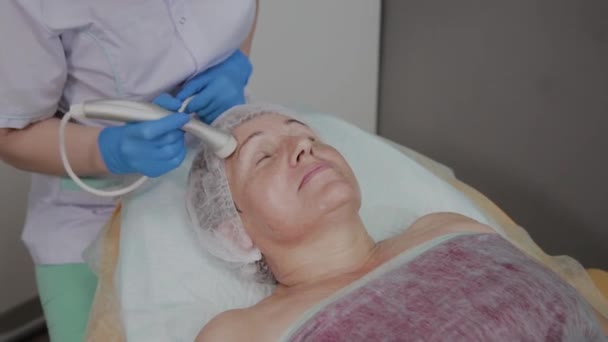 Профессиональный косметолог проводит процедуру для пожилой женщины с микротоками в отделении косметологии
. - Кадры, видео