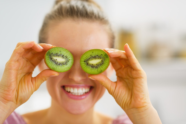 Happy young woman making eyes with kiwi slices - Fotó, kép
