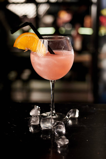 close-up shot of topical pink cocktail with orange on wooden bar counter - Foto, afbeelding