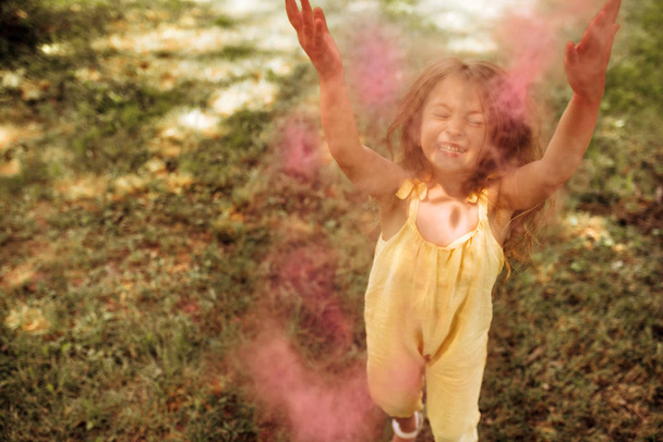 幸せなブロンドの小さな女の子は、想像力やおとぎ話の概念のための魔法のピンクのほこりで公園で遊んでいます。彼女の誕生日パーティー中に公園でピンクの粉で遊ぶ美しい子供. - 写真・画像