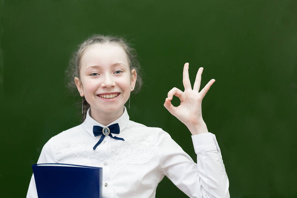 Successful teen schoolgirl smiling holding up her hand. Girl student shows a hand sign that she is fine Passed the exam for a good grade - Фото, изображение