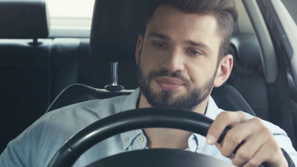 selective focus of handsome man holding steering wheel and waving while holding paper in car  - Footage, Video