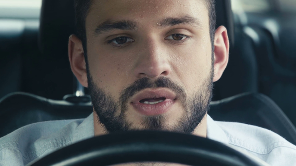 blízký zpocený muž gestikulací při sezení v autě a přidržením volantu  - Záběry, video