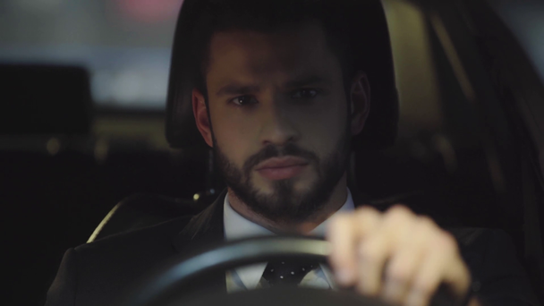 Selektiver Fokus eines gutaussehenden bärtigen Mannes im Anzug, der während der Autofahrt das Lenkrad hält  - Filmmaterial, Video