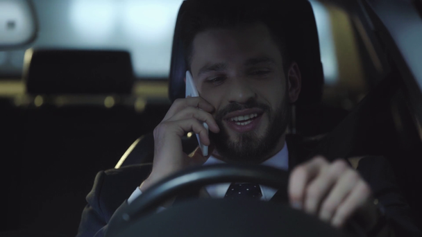 selectieve focus van knappe man in pak rijden auto, het nemen van smartphone, praten en glimlachen, dan kijken naar venster  - Video