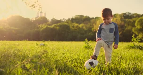 Boy standing on the grass with a soccer ball at sunset - Footage, Video