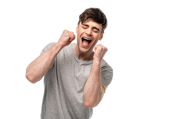 opgewonden jonge man toont winnaar gebaar met gesloten ogen geïsoleerd op wit - Foto, afbeelding