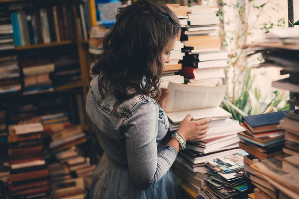 Μια όμορφη νεαρή γυναίκα στο βιβλιοπωλείο, ανοίγοντας ένα βιβλίο - Φωτογραφία, εικόνα