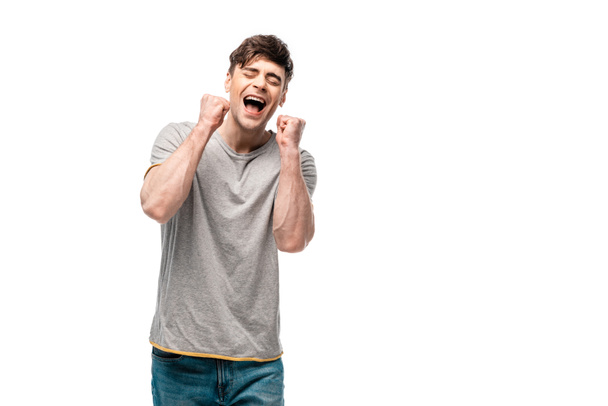 gelukkige jonge man toont winnaar gebaar met gesloten ogen geïsoleerd op wit - Foto, afbeelding