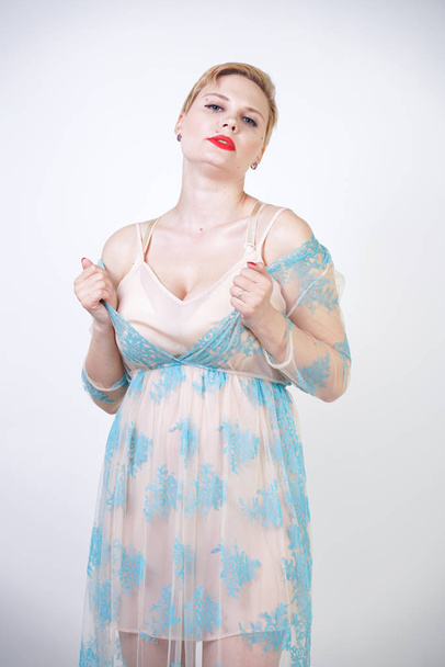 pretty cute blonde woman with short hair and plus size body wearing long transparent blue lace dress. stylish fashionable adult girl in cute nightgown on white studio background alone. - Photo, Image