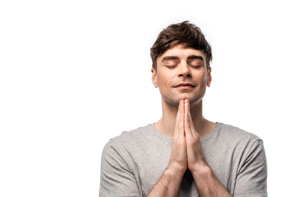pensive man with closed eyes showing pray gesture and smiling isolated on white - Foto, immagini