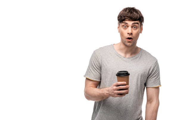 surprised young man looking at camera while holding coffee to go isolated on white - Photo, Image
