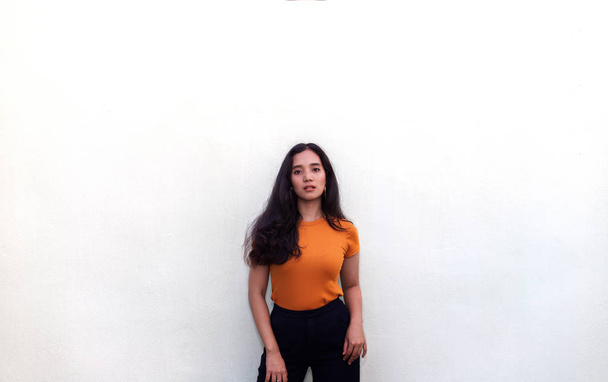 Duvarda poz veren turuncu tişörtlü genç kadın. - Fotoğraf, Görsel