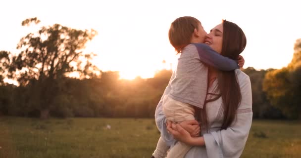 Chłopiec przytulanie matka o zachodzie słońca w lecie, kochający syn i szczęśliwą rodzinę dotykając - Materiał filmowy, wideo